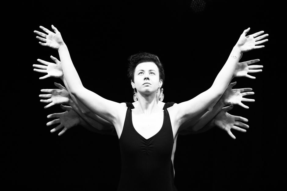 Black and white surreal stage performance featuring a performer with multiple hands.