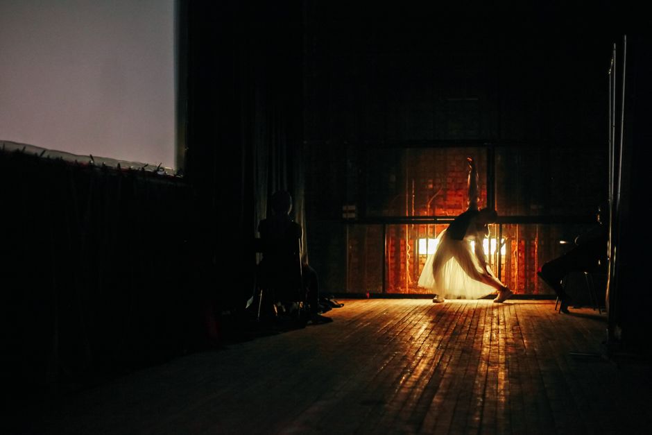 A ballet dancer elegantly posing backstage with dramatic lighting casting a silhouette.