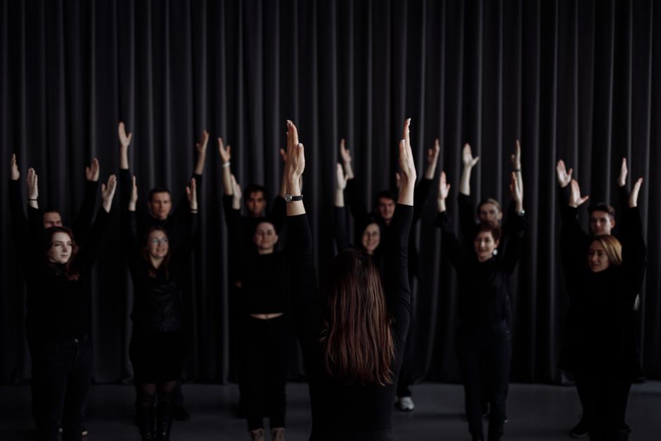A group of performers rehearsing a contemporary dance with raised arms indoors.